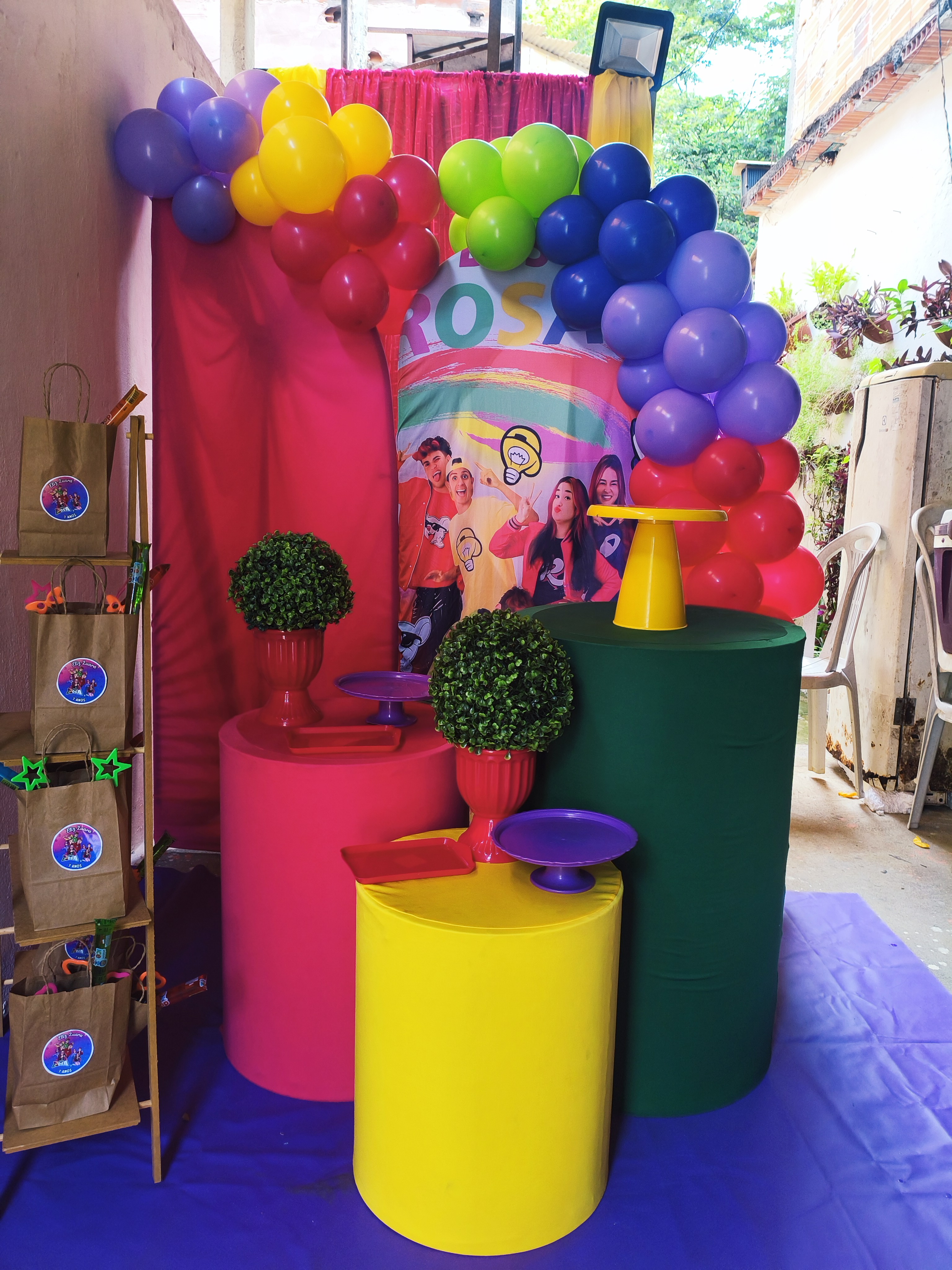 Festa com balões e mesas em amarelo, rosa, verde e roxo
